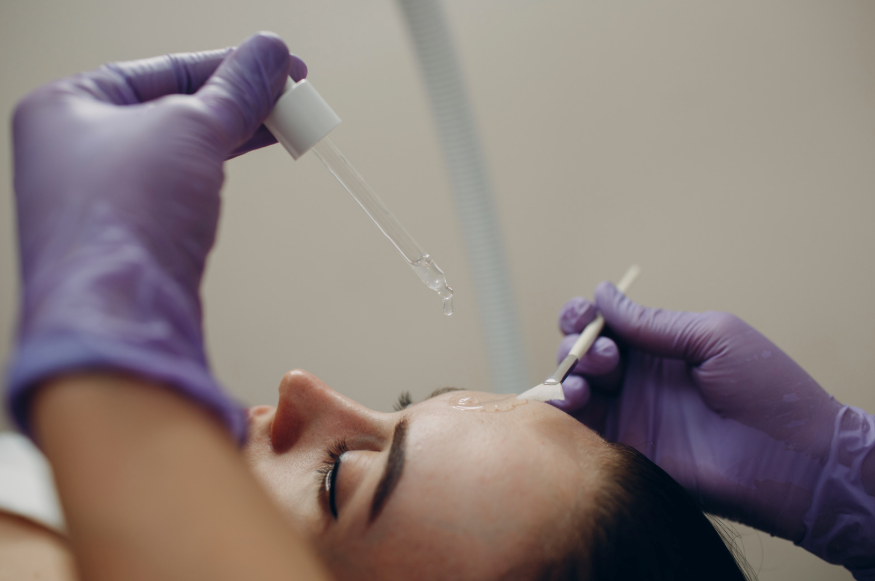 Behandler påfører et flydende produkt på en kundes pande med pipette og spatel